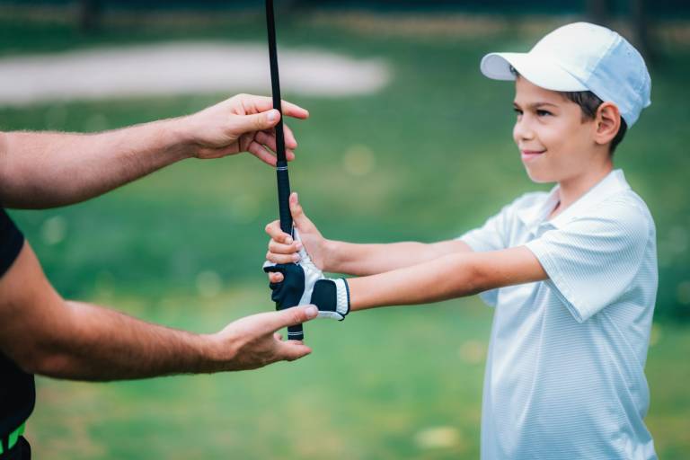 Golf Instructor adjusting young boy’s grip